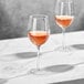 Two Della Luce Maia wine glasses on a marble table with wine in them.