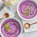 Two bowls of purple soup with white cream and green sprouts, spoons, and flowers.