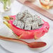 A half of a cut Fresh Pink Dragon Fruit with black seeds and a spoon.