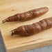 Two long brown sticks of fresh yuca on a wooden surface.