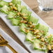 A plate of cucumber salad with nuts on a table next to a fork and a glass.