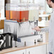 A man pouring liquid into a Crathco refrigerated beverage dispenser with a glass.