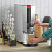 A hand holding a faucet pours hot water into a paper cup.