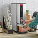 A woman using a Grindmaster hot water dispenser to fill a paper cup.