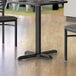 A black Lancaster Table & Seating standard height column table base with a table top, plate, and cup on it.