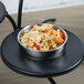A bowl of pasta on a black surface with a Vollrath round adapter plate.