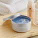 A silver tin of blue cream on a wood surface.