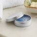 A close-up of a silver metal tin with a screw top filled with blue cream.