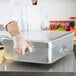 A chef in gloves using a Vollrath aluminum double roaster pan on a counter.