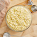 A bowl of Golden Dipt Hush Puppy Mix dough with a spoon and a measuring spoon.