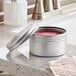 A silver container with a lid open on a counter containing red liquid.