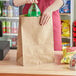 A person putting a green bottle of soda into a brown Choice 1/6 paper barrel sack.