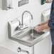 A person washing their hands under a Regency wall-mounted hand sink with a gooseneck faucet.