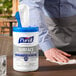 A person's hand holding a white plastic bottle of Purell Professional Surface Disinfecting Wipes.