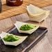 A Tablecraft disposable wood boat with two small bowls of food on it.