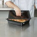 A person using a black Cambro polycarbonate lid to cover a container of food.