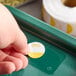 A hand holding a roll of Noble Products Tuesday Day of the Week stickers on a green tray.