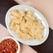 A Carlisle bone melamine oval platter with a plate of chips on a table.