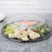 A clear plastic round high dome lid on a tray of vegetables.