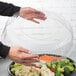 A person holding a WNA Comet clear plastic container filled with broccoli and tomatoes.