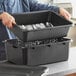 A man holding a black Choice polypropylene drain box filled with silverware.