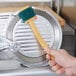 A hand using a yellow Carlisle Sparta Easy Slicer Cleaning Tool to clean a meat slicer.