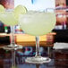 Two Anchor Hocking margarita glasses filled with drinks on a bar counter.
