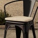 A black Lancaster Table & Seating chair with a tan fabric cushion on top.