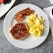 A white Arcoroc porcelain plate with a bagel, eggs, and bacon on it.