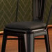 A black vinyl cushion on a Lancaster Table & Seating Alloy Barstool.