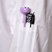 A white Chef Revival chef coat with black piping and a purple pen in the pocket.
