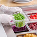 A person in gloves holding a Carlisle clear polycarbonate food pan of peas on a counter.