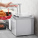 A person using a ServSense stainless steel condiment dispenser to pour sauce into a basket of fried chicken.