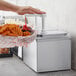 A person using a ServSense stainless steel condiment dispenser to pour ketchup onto a basket of waffle fries.