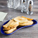 A Tuxton cobalt blue china crescent dish with potato wedges on a table.