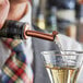 A man using an Acopa copper liquor pourer to pour liquid into a glass.