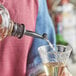 A person using an Acopa black tapered liquor pourer to pour liquid into a glass on a table.