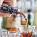 A hand using an Acopa copper angled liquor speed pourer to pour rum into a glass of brown liquid with ice.