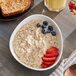 A bowl of Bob's Red Mill gluten-free oatmeal with strawberries and blueberries on a table.