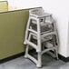 A Rubbermaid restaurant high chair with wheels sits in front of a wall.