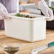 A person in white gloves using tongs to serve salad from a white Cambro food container.