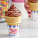A chocolate ice cream cone in a brown JOY flat bottom cone on a counter.