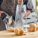 A person in gloves holding a Choice plastic bag of bread on a table.