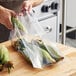 A hand holding a Choice heavy-duty plastic bag filled with corn on the cob.