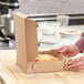 A person putting a Kraft bakery box of food on a table.