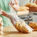 A woman in a green apron putting a bag of bread in a Choice plastic food bag.