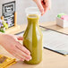 A hand holding a green bottle of liquid with a lid being put on it.