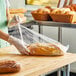 A woman in a green apron holding a Choice standard-duty plastic food bag filled with a loaf of bread.