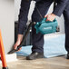 A man using a Makita handheld cordless vacuum to clean a floor.