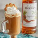 A glass mug of brown liquid with a cookie on top next to a bottle of Monin Premium Gingerbread Flavoring Syrup.